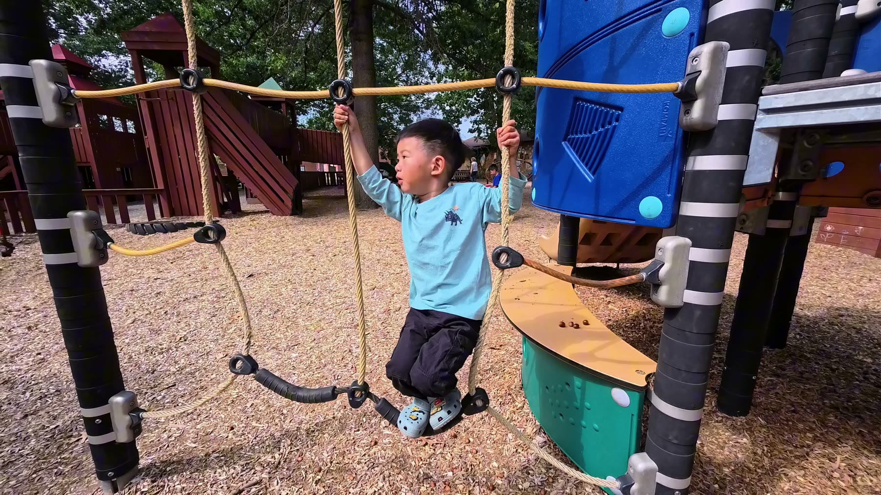 Spencer climbing a rope bridge at a playground