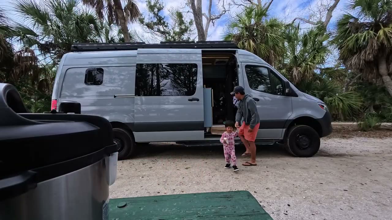 Our white Sprinter van parked under palm trees by the water in Florida